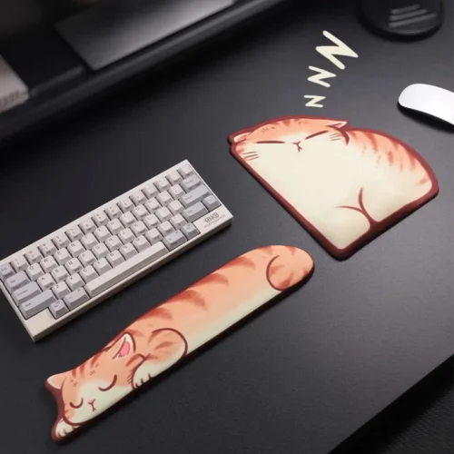 Sleepy Orange Tabby Wrist Rest Set showing a sleeping cat-shaped keyboard palm rest and a cushioned wrist-support mouse mat on a dark desk.