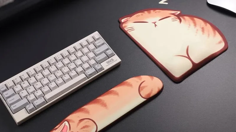Sleepy Orange Tabby Wrist Rest Set showing a sleeping cat-shaped keyboard palm rest and a cushioned wrist-support mouse mat on a dark desk.