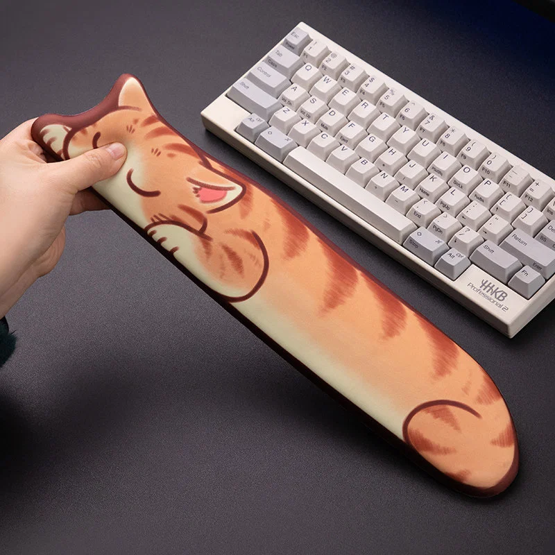 Sleepy Orange Tabby Keyboard Wrist Rest held and squeezed by hand to show flexible, cushioned support beside a mechanical keyboard on a desk.
