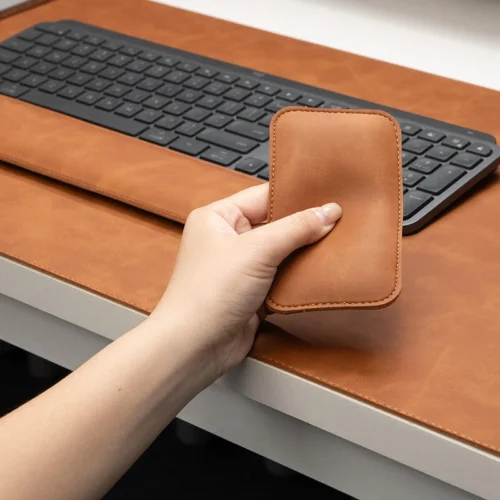 Hand holding the matching mouse wrist rest from the executive leather desk pad set, showing compact shape and coordinated leather finish