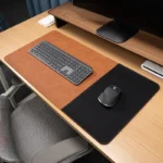 Caramel brown leather desk mat with a black fabric mouse zone in a clean office desktop setup with keyboard and mouse