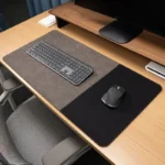 Taupe executive leather desk mat with a black fabric mouse section displayed on a light wood office desk with keyboard and mouse