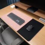 Blush pink leather desk mat with black fabric mouse area displayed on a wood desk with keyboard and mouse in an office setting