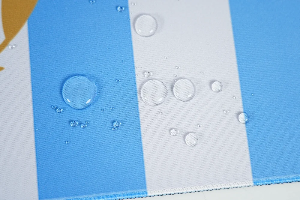 Spill Resistant Argentina Desk Mat Surface Spill-resistant Argentina football desk mat surface with water droplets on blue-white fabric and stitched edge for easier cleanup