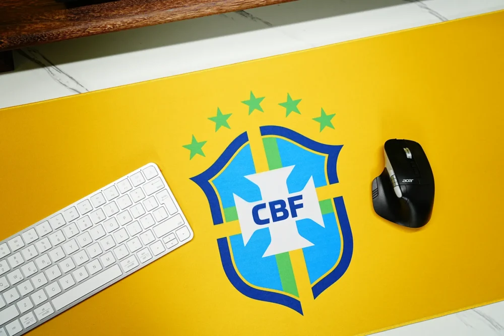 Brazil football mouse pad close-up showing vivid yellow fabric, clear crest artwork, keyboard placement, and smooth mouse space