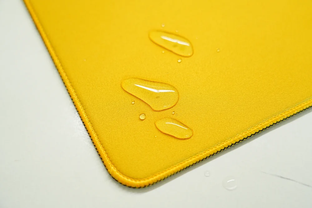 Spill-resistant Brazil desk mat surface with water droplets staying on the yellow fabric instead of soaking in quickly