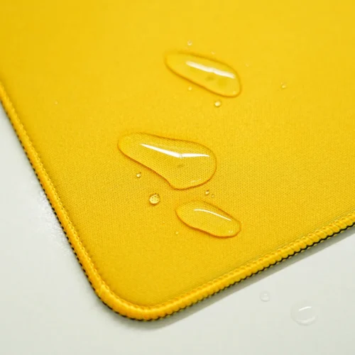 Spill-resistant Brazil desk mat surface with water droplets staying on the yellow fabric instead of soaking in quickly