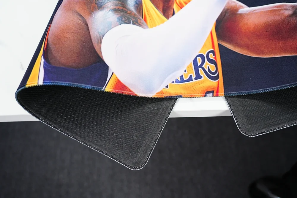 Kobe Bryant mouse pad lifted to show anti-slip rubber base, stitched edges, and flexible desk mat structure