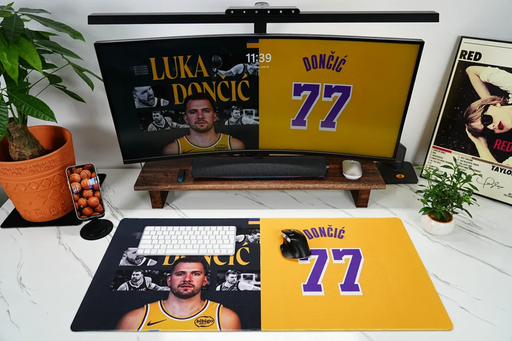 Lakers 77 fan gaming desk mat shown in a styled workspace with monitor, keyboard, mouse, plants, and basketball-inspired decor