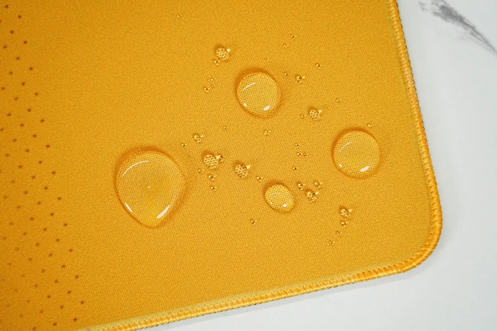 Water drops resting on the desk pad surface, showing water-resistant fabric that helps protect the artwork during small spills