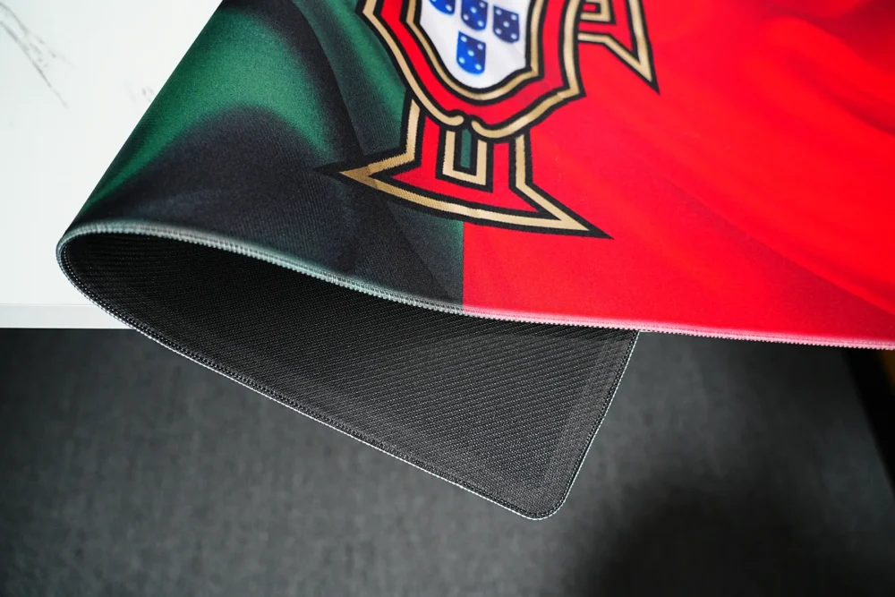Portugal football desk mat lifted to show stitched edges, flexible fabric, and textured rubber base for stable desk use