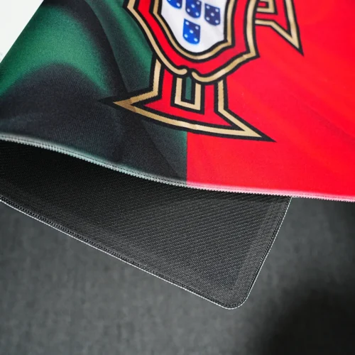 Portugal football desk mat lifted to show stitched edges, flexible fabric, and textured rubber base for stable desk use