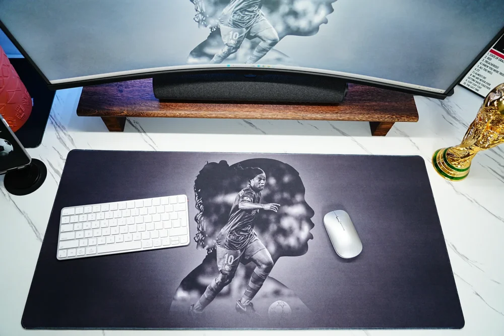 Ronaldinho Barcelona desk mat used with keyboard, mouse, matching monitor wallpaper, and World Cup trophy decor in a fan desk setup