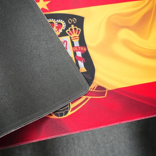 Spain football desk mat lifted to show black anti-slip rubber backing, flexible material, and stitched edge construction.