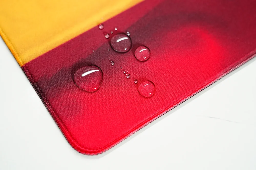 Spill-resistant Spain football team desk mat surface with water droplets beading on the fabric and stitched edge detail.