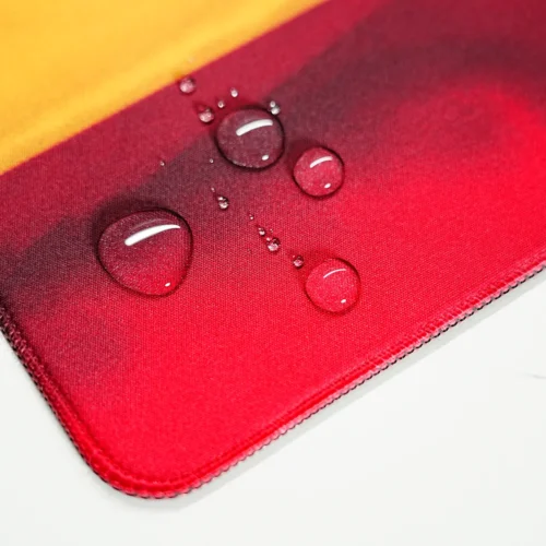 Spill-resistant Spain football team desk mat surface with water droplets beading on the fabric and stitched edge detail.