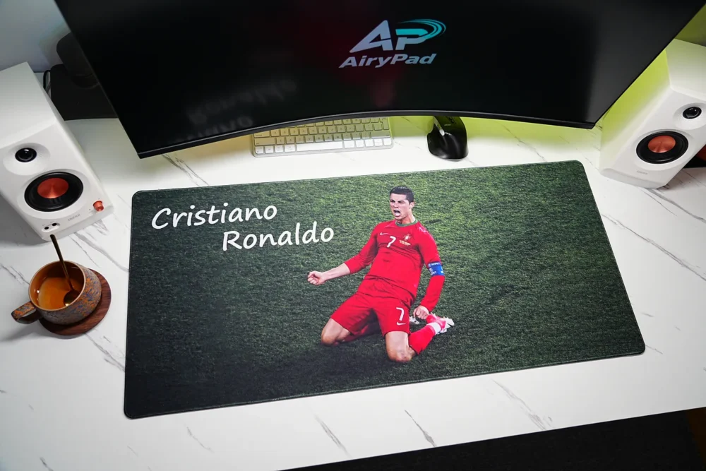 Overhead view of Cristiano Ronaldo mouse pad beneath a curved monitor with keyboard, mouse, speakers and coffee cup