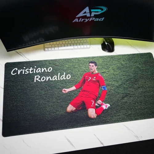 Overhead view of Cristiano Ronaldo mouse pad beneath a curved monitor with keyboard, mouse, speakers and coffee cup