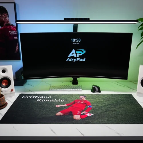 Cristiano Ronaldo football desk mat in a complete green-lit setup with curved monitor, speakers, plants and Ronaldo wall art