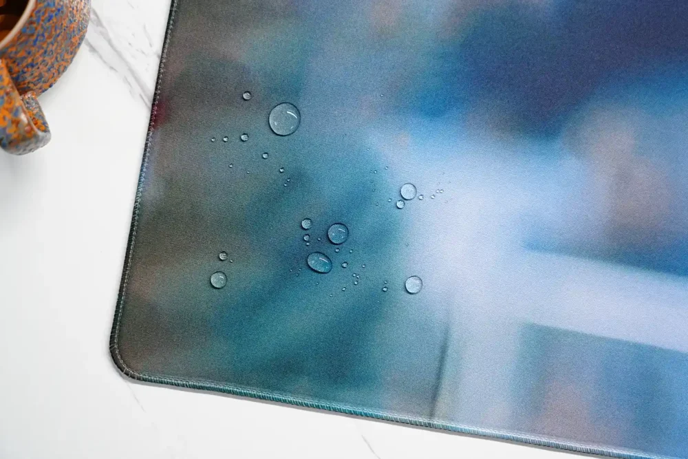 Water droplets beading on the David Beckham desk mat spill-resistant fabric beside the stitched edge