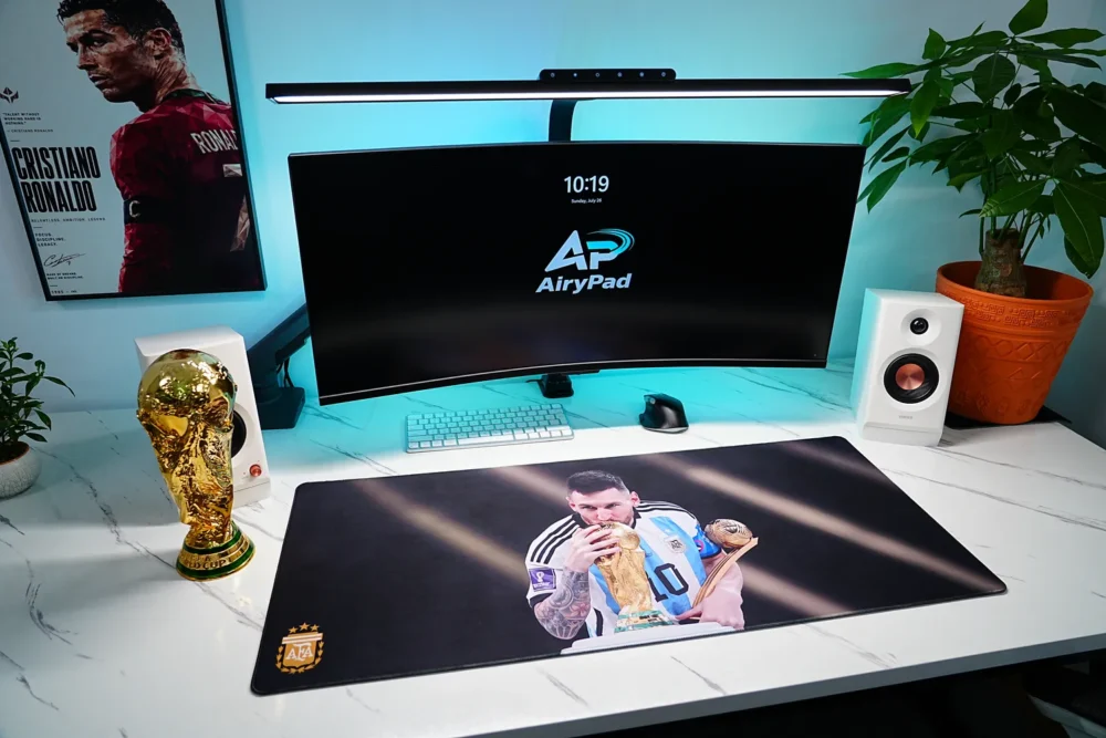Angled workstation with Lionel Messi World Cup desk mat, curved monitor, keyboard, speakers, plant and trophy