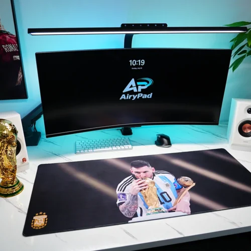 Angled workstation with Lionel Messi World Cup desk mat, curved monitor, keyboard, speakers, plant and trophy